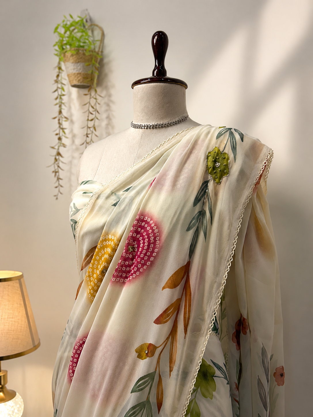 Elegant ivory organza saree with colorful floral and circular motifs draped on a mannequin in a premium studio setting with warm lighting.