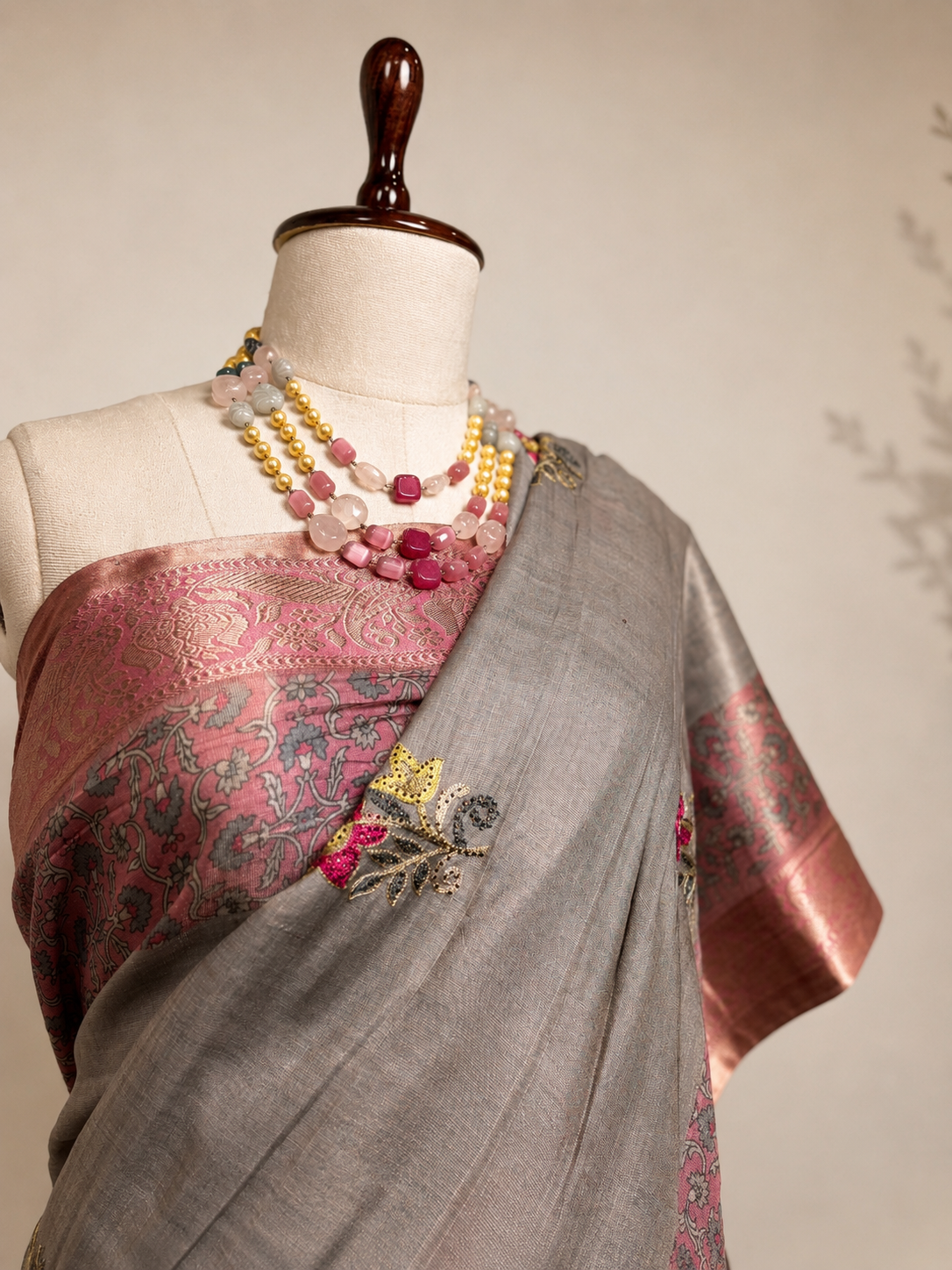 Grey Khadi Silk saree with pink woven border and floral motifs displayed on mannequin in elegant studio setup.
