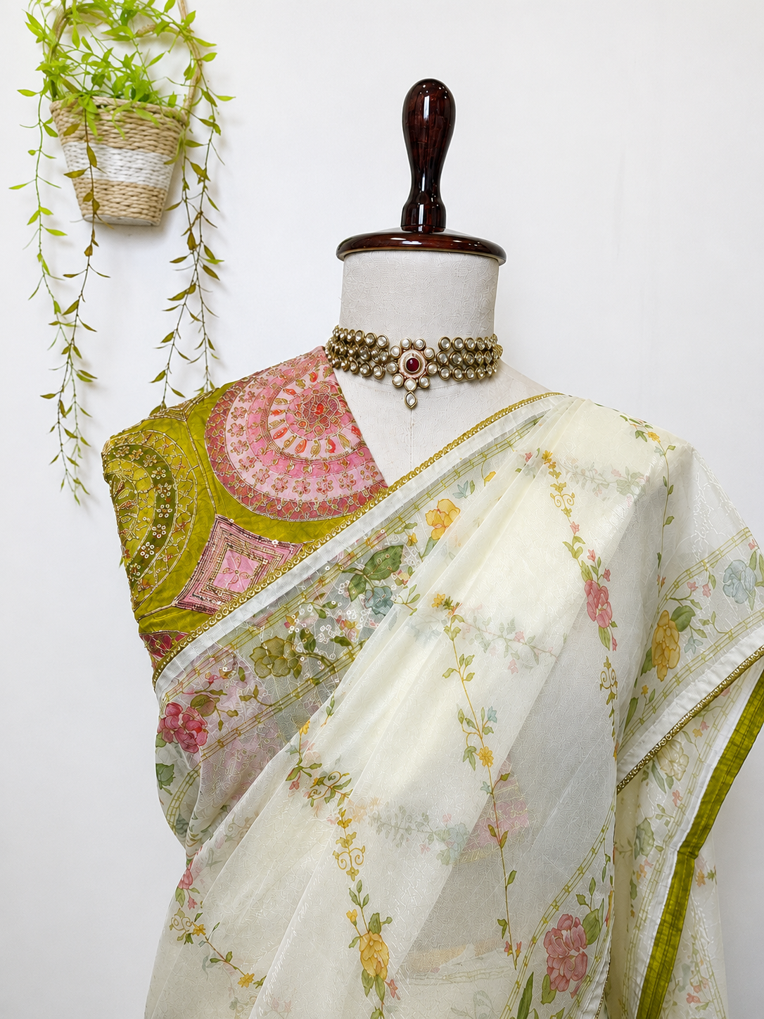Ivory saree with floral prints and a heavy embroidered green designer blouse on a mannequin in a premium studio setting.