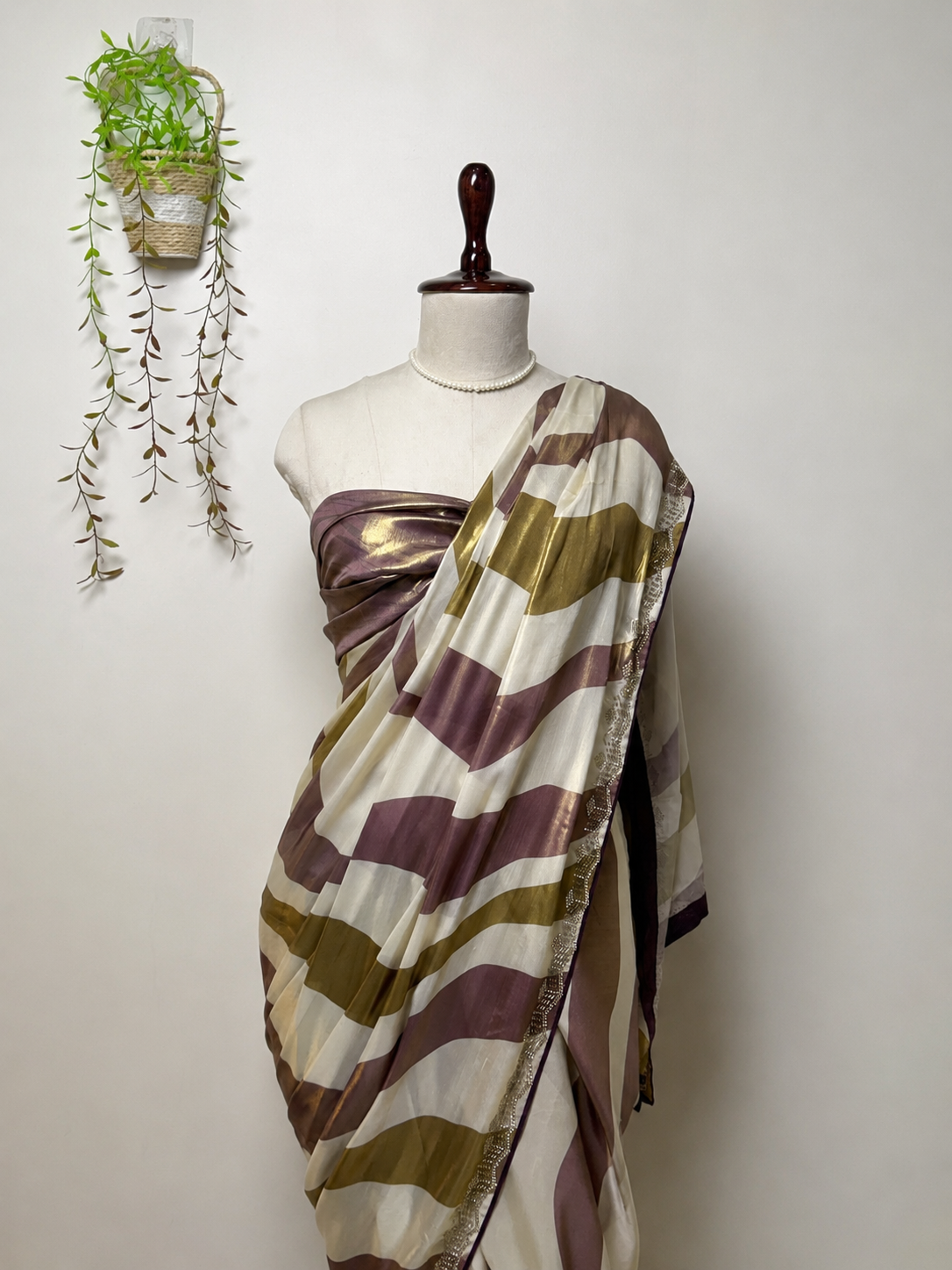 Elegant pearl white modal silk saree with mauve and olive metallic stripes, shimmering border, and soft flowing drape displayed on mannequin for festive and party wear styling.