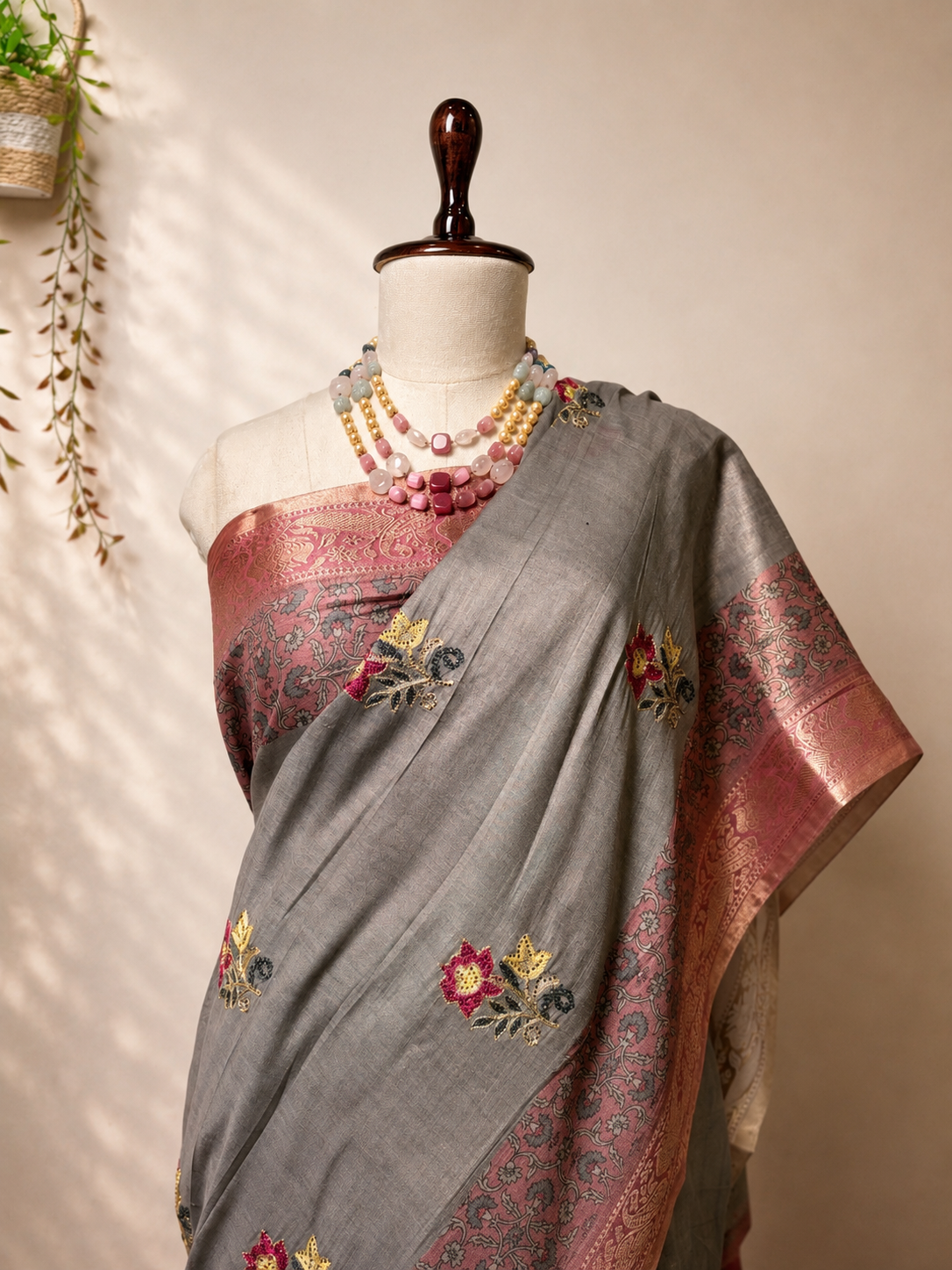 Grey Khadi Silk saree with pink woven border and floral motifs displayed on mannequin in elegant studio setup.
