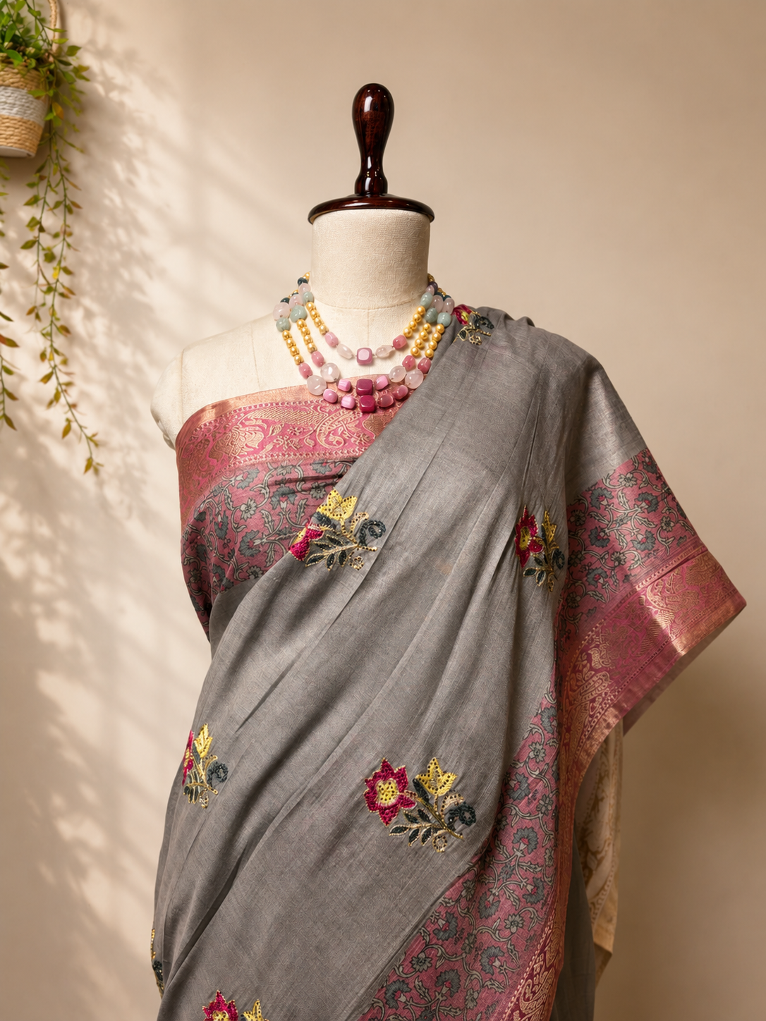 Grey Khadi Silk saree with pink woven border and floral motifs displayed on mannequin in elegant studio setup.
