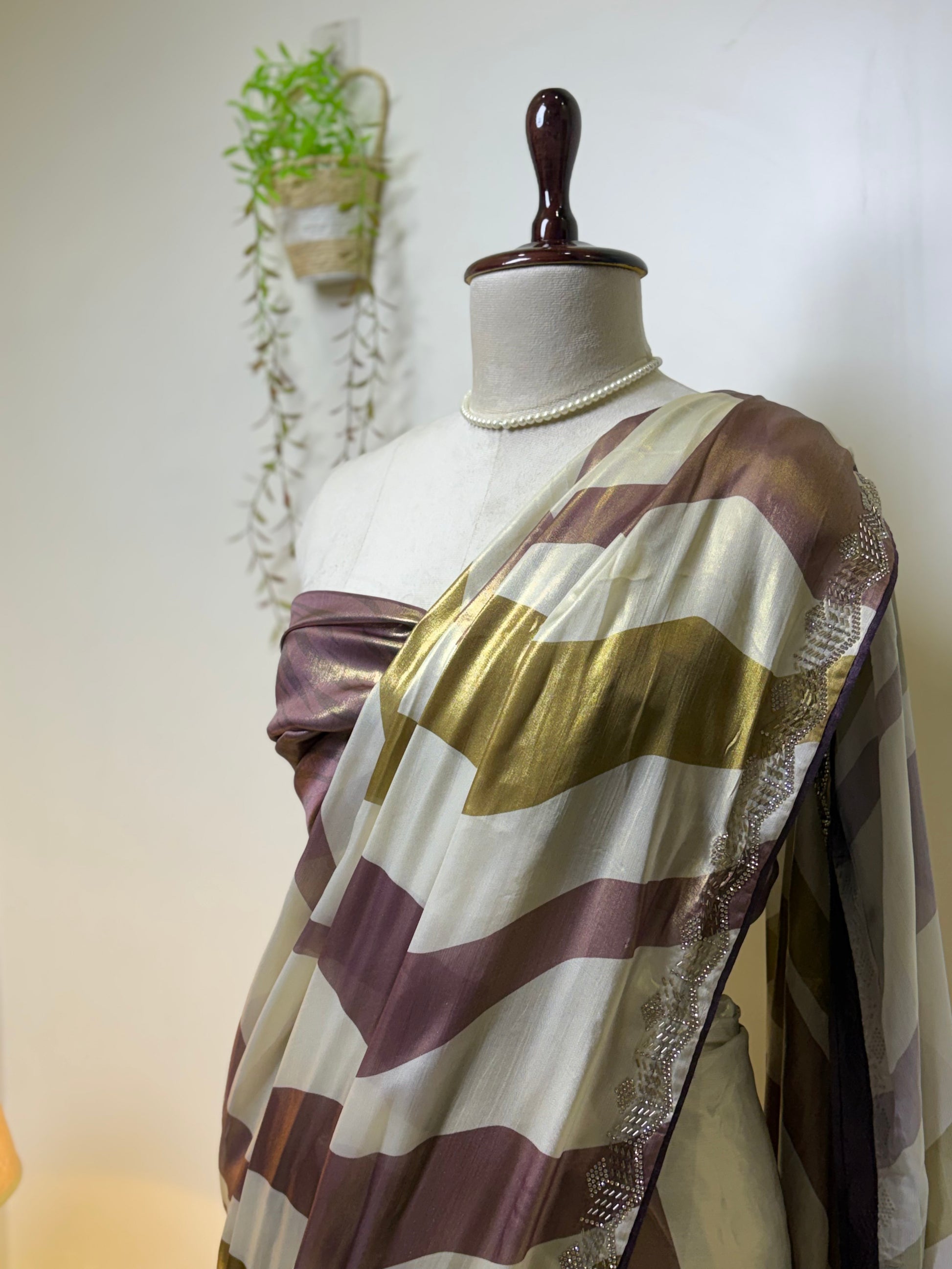 Elegant pearl white modal silk saree with mauve and olive metallic stripes, shimmering border, and soft flowing drape displayed on mannequin for festive and party wear styling.